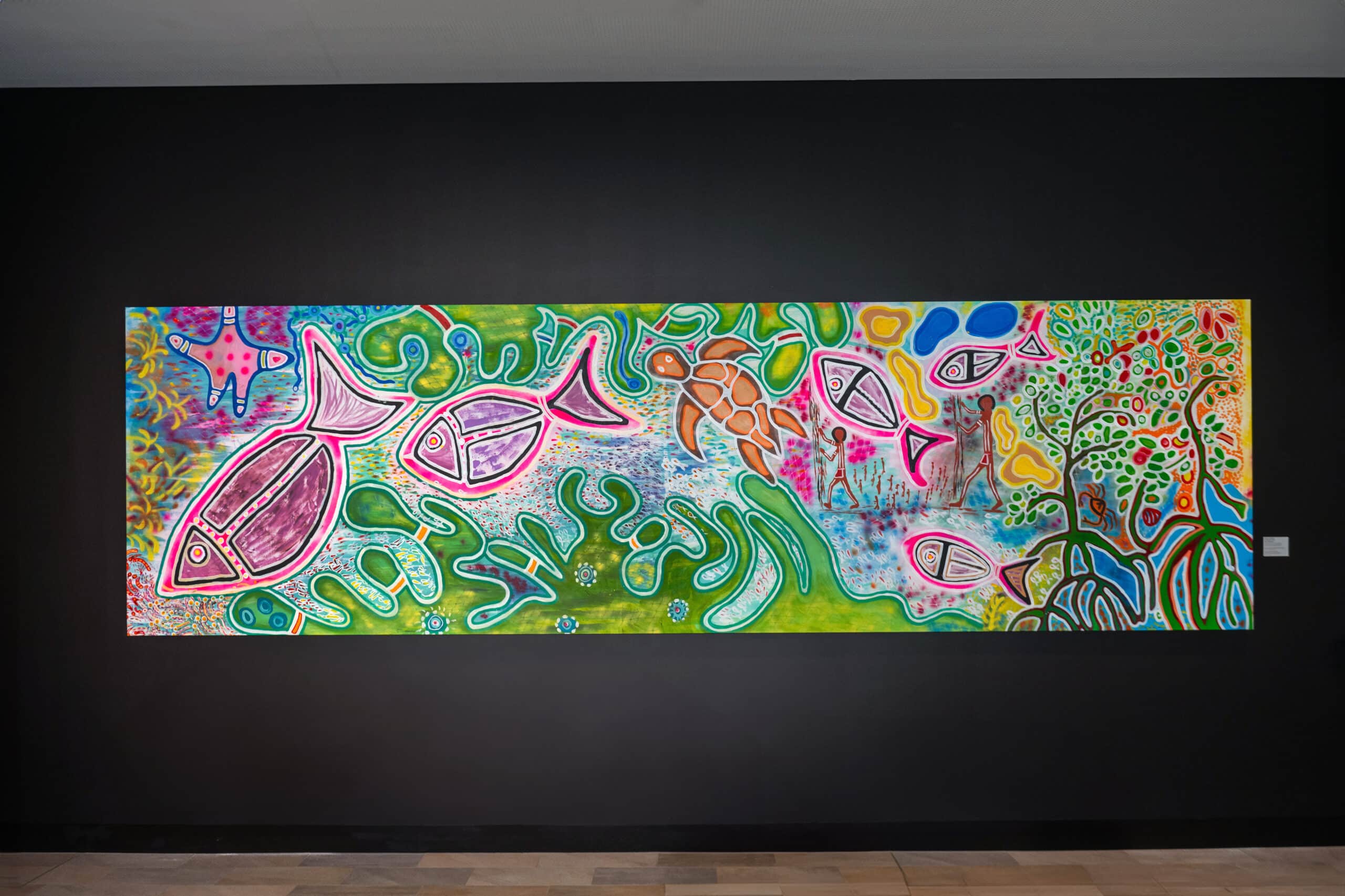 Reef Connections’ by Elverina Johnson — a vibrant painting featuring marine life such as fish and a turtle, abstract reef-inspired patterns, mangroves, and depictions of First Nations people hunting, reflecting cultural and environmental connections.