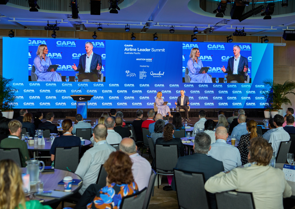 A large audience in the Trinity Room at Cairns Convention Centre watches a panel session on stage at the CAPA Airline Leader Summit, with a wide LED screen displaying event branding and the discussion taking place.