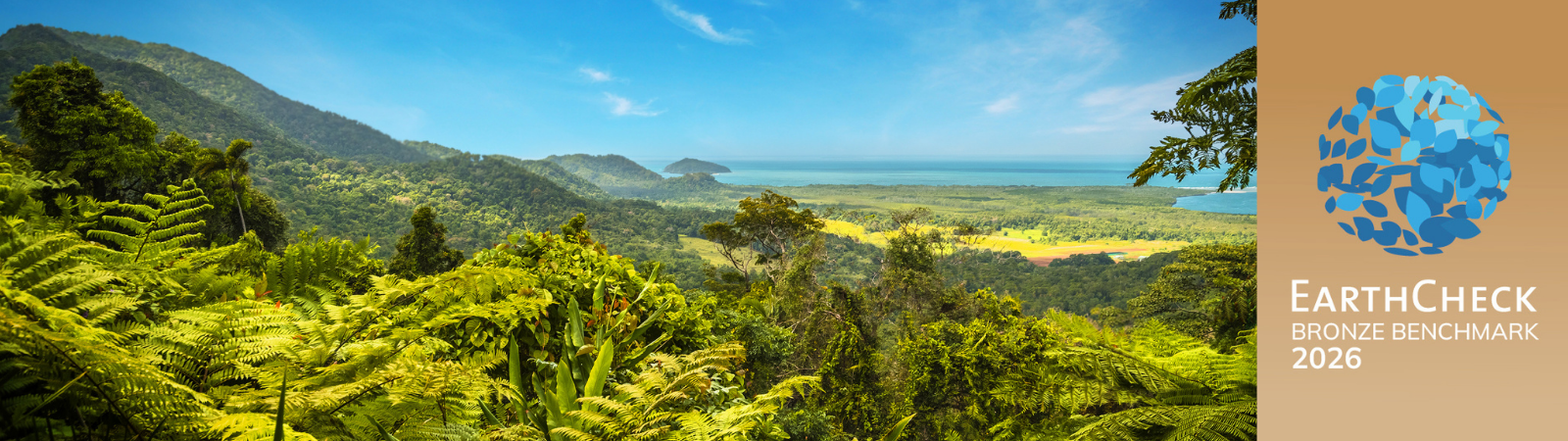 Panoramic view of lush tropical rainforest leading to the coastline under a bright blue sky, with the EarthCheck Bronze Benchmark 2026 certification badge displayed on the right.