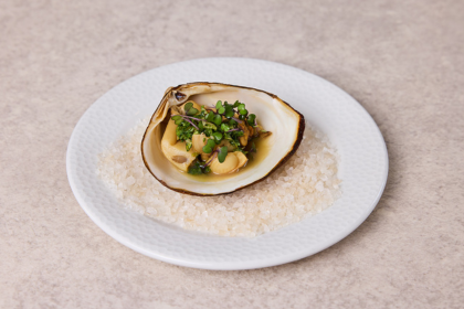 Storm clam served in shell with native garnishes, presented on a white plate of coarse salt.