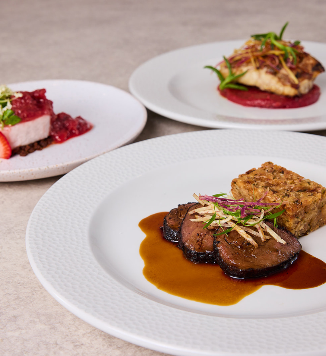 Kangaroo served with a dark jus and taro mousse, presented on a white plate, with mangrove jack and berry desserts visible behind.